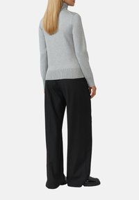 Un pull col roulé gris avec un ourlet et des poignets côtelés, associé à un pantalon large noir et des chaussures noires, vu de dos.