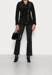 Czarna zamszowa kurtka z asymetrycznym zamkiem, pasek w talii i pagonami. Połączona z czarnymi spódnicami w kształcie dzwonu i teksturowaną czarną torebką.