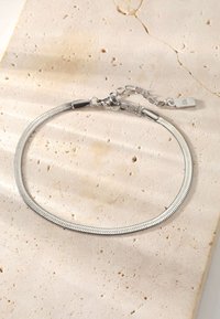 Silver chain necklace with a flexible, textured design and a lobster clasp. Features a short length and a small tag at the clasp.