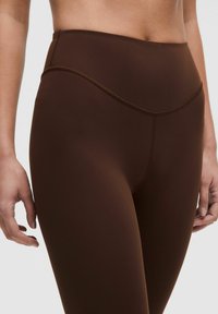 Bruine high-waisted legging gemaakt van rekbaar materiaal, met een gladde textuur en subtiele naden langs de taille en benen.