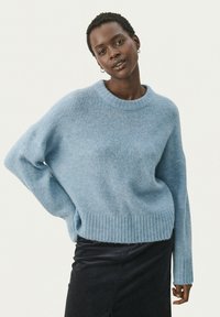 Pull en tricot bleu clair avec un ourlet et des poignets côtelés, présentant une coupe décontractée et un col rond, fabriqué à partir d'un matériau doux et texturé.