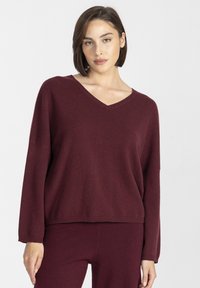 Bordowy sweter w serek z miękkiego materiału, o luźnym kroju, z długimi rękawami i żeberkowym wykończeniem. W zestawie z pasującymi spodniami.