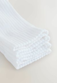 Pile de serviettes blanches en coton côtelé pliées sur une surface claire, montrant la texture et les bords superposés.