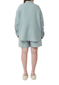 Lichtblauwe, gestructureerde blouse gecombineerd met bijpassende shorts. De outfit heeft een relaxte pasvorm en heeft een kraag en lange mouwen.