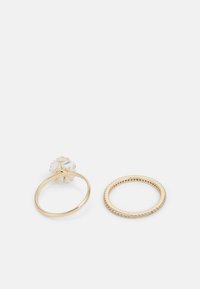 Les bagues en ton doré incluent une bague groupée avec une pierre précieuse claire et une bande texturée ornée de petites pierres claires.