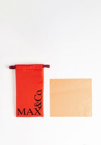 Pungă din material roșu cu șnururi, având inscripția "MAX & Co." în negru, lângă un pătrat de culoare bej deschis cu litere în relief care spun "MAX & Co.".