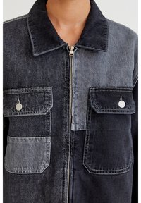 Denimjakke med spredt krave, med et tofarvet design i mørkegrå og lysegrå, lynlåslukning og to brystlommer med klapper.