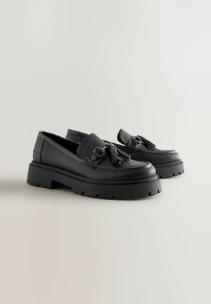 Černé kožené loafers s texturovaným povrchem, s ozdobou ve tvaru střapce a robustní gumovou podrážkou s drsným vzorkem.