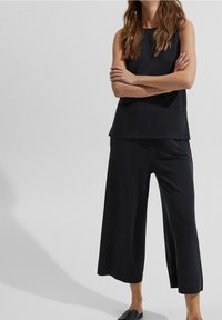 Top nero senza maniche abbinato a pantaloni neri a gamba larga. Tessuto liscio, vestibilità ampia, senza modelli o hardware visibili.