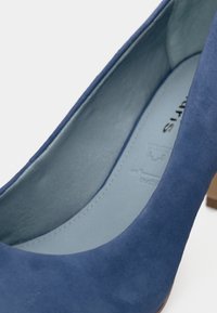 Gros plan de l'intérieur et de la partie supérieure d'une chaussure à talons hauts en daim bleu avec une semelle intérieure gris clair et un talon en bois.