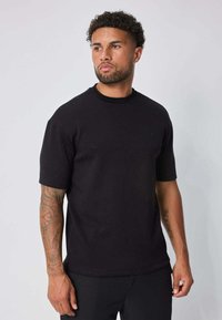 T-shirt noir à manches courtes en tissu doux, avec un col rond et de subtils motifs texturés parsemés sur toute la surface.