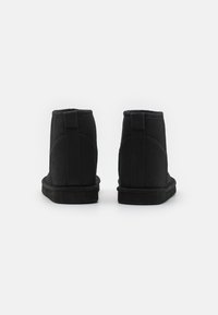 Botas negras hasta el tobillo hechas de ante, con una textura suave, puntera redonda, un diseño sin costuras y una suela de goma plana con acentos mínimos.