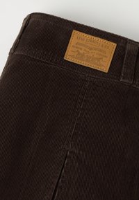 Pantalon en velours côtelé brun foncé avec une étiquette beige Levi's cousue à la ceinture affichant le logo et le texte de la marque.