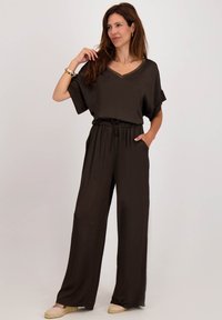 Bruine jumpsuit met een V-hals, korte mouwen, elastische tailleband en zijzakken. Zacht, lichtgewicht stof met flowy wijde broekspijpen.