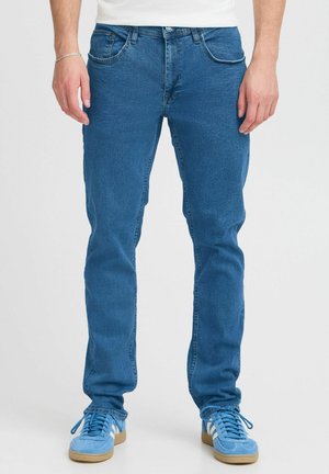 Blå denim jeans med smal passform, med fem lommer, knappelukking og subtil falming på beina. Kombinert med lyseblå sneakers.