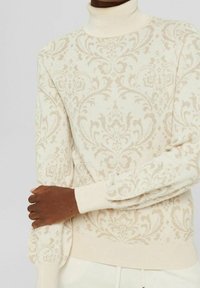 Krämfärgad polokrage-tröja med intrikat beige damaskmönster. Figursydd silhuett och räfflade ärmslut. Mjuk stickad textur, lätt design.