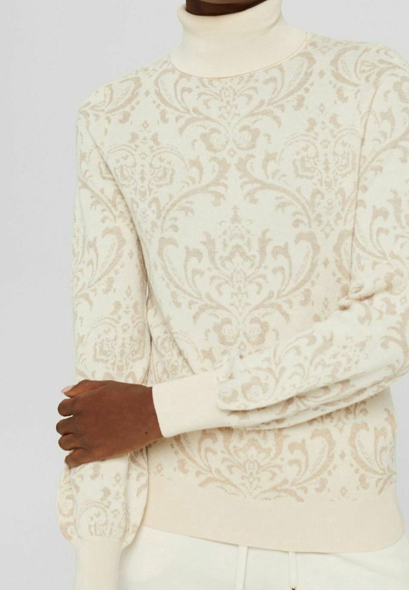 Krämfärgad polokrage-tröja med intrikat beige damaskmönster. Figursydd silhuett och räfflade ärmslut. Mjuk stickad textur, lätt design.