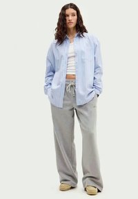 Ανοιχτό μπλε πουκαμίσα με ρίγες, λευκή μπλούζα, γκρι φόρμες και μπεζ αθλητικά παπούτσια. Ανετη εφαρμογή με ορατή λεπτομέρεια τσέπης στην πουκαμίσα.