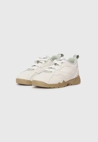 Un paio di sneakers sportive bianche e beige con lacci, pannelli laterali in rete e linguette su uno sfondo bianco.