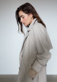 Beige uldblanding frakke med en afslappet pasform, der har store knapper, sidelommer og ribbede manchetter i en lysere nuance af beige.