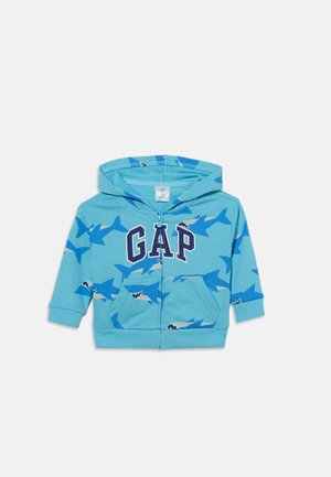 Világoskék kisgyermek kapucnis pulóver teljes zipzárral, sötétkék "GAP" betűkkel és sötétkék cápa mintával a szöveten.