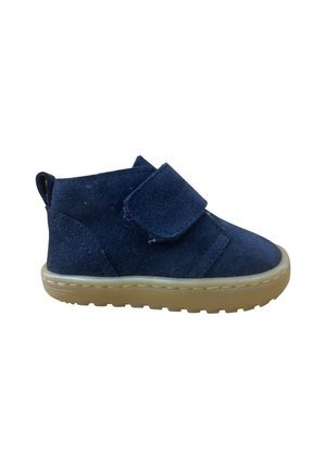 Zapato para niño pequeño de ante azul marino con correa de velcro y suela de goma beige, vista lateral sobre fondo blanco.