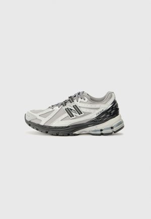 Zapatilla de running New Balance 1906R en gris y negro con parte superior de malla, suela acolchada y diseño con cordones, mostrada de lado sobre fondo blanco.