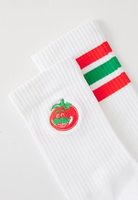 Chaussettes blanches avec une texture côtelée, ornées d'une tomate rouge brodée avec une moustache verte et des rayures colorées en rouge et vert.