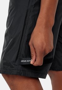 Pantaloni corti neri realizzati in tessuto leggero con una finitura testurizzata. Presentano un'etichetta CEPLX ACTIVE visibile e un dettaglio regolabile in Velcro.