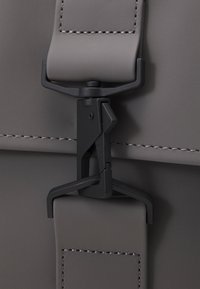 Sac gris avec une surface texturée, doté d'une fermeture à clip en plastique noir et d'un détail de couture contrastant le long des bords.