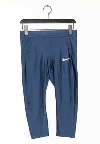 Námořnické modré krátké legíny Nike s bílým logem swoosh, visící na černém ramínku na bílém pozadí.