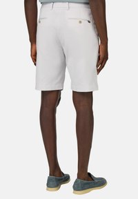 Shorts gris clair avec une coupe ajustée, dotés de poches arrière avec des boutons. Portés avec des mocassins en daim bleus.