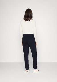 Navy sweatpants with an elastic waistband, side pockets, and tapered legs, paired with a light long-sleeve top and white sneakers.