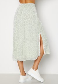 Falda midi verde claro con un patrón de flores, cinturilla elástica y una abertura lateral. Combinada con zapatillas blancas sobre un fondo simple.