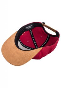 Red cap with a tan suede brim, featuring a black interior band with logo accents. Visible stitching and a structured shape.