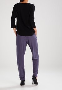 Svart överdel med trekvartsärm i kombination med lösa, lila byxor. Utseendet fulländas med stiliga svarta högklackade skor.