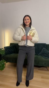 Crèmekleurig fleecejack met een gouden ritssluiting, een capuchon en geribbelde manchetten, gecombineerd met grijze broek met wijde pijpen en zwarte schoenen.