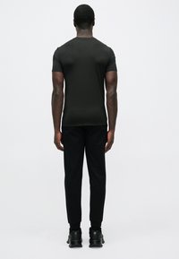 Melna īsroku T-krekls kopā ar melnām sporta biksēm, kas izceļas ar piegulošu dizainu un gludu tekstūru. Melnas sporta kurpes noslēdz izskatu.