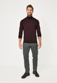 Bordeauxroter Rollkragenpullover in figurbetontem Design, kombiniert mit strukturierten grauen Hosen und schwarzen Schnürschuhen. Schlichtes, modernes Styling.