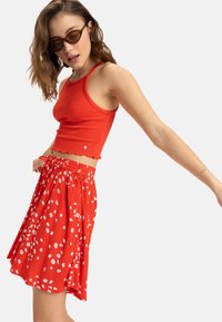 Röd ribbad crop top med vågig fåll, parat med en röd kjol som har små vita blommönster och elastisk midja.