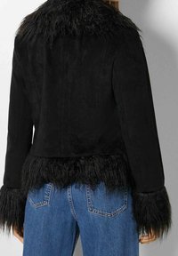 Giacca nera in pelliccia sintetica con colletto e polsini testurizzati, caratterizzata da un corpo in suede e orlo frangiato. Abbinata a jeans in denim blu.
