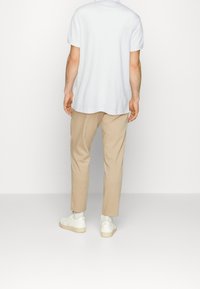 Vit bomullströja med rundad nederkant, matchad med beiga skräddarsydda byxor och vita sneakers. Minimalistisk design utan mönster eller detaljer.