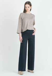 Beige lyhytselkäinen neulepaita pitkillä hihoilla ja sivurei'illä, yhdistettynä merenkulku sinisiin levealahkeisiin housuihin ja kuvioituihin tasapohjaisiin kenkiin. Yksinkertainen ja jämäkkä muotoilu.