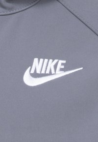 Grijze sportstof met een wit geborduurd Nike-logo. Het ontwerp bevat een ronde kraag en een soepele textuur.