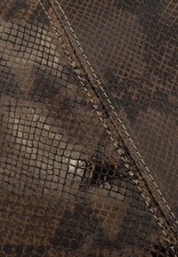 Brązowy materiał z imitacji węża o teksturowanej powierzchni, z wzorzystym wzorem i widocznym jasnym szwem.