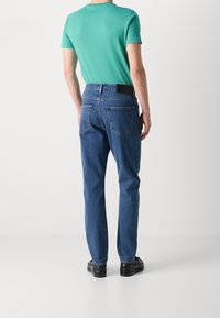 Grön t-shirt för män i kombination med blå denimjeans. Jeanssen har en klassisk femficksdesign och rak benpassform, med en snygg finish.