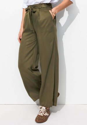 Pantalons larges vert olive avec une taille à nouer, texture lisse et poches latérales profondes, associés à des baskets imprimées léopard marron.