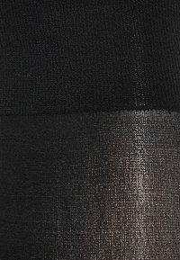 Sorte strømpebukser med en textureret strik øverst, der glider over i en glat, blank finish nederst, hvilket skaber en gradient effekt.