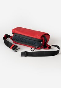 Rode en zwarte heuptas met dubbele ritscompartimenten en een verstelbare zwarte riem met een plastic zijslot dat niet is vastgeklikt op een witte achtergrond.