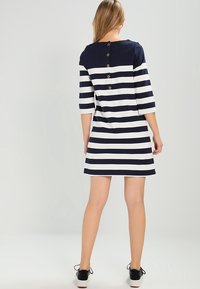 Robe rayée bleu marine et blanche avec des manches trois-quarts, un col rond et des détails de boutons le long du dos, fabriquée en doux tissu en mélange de coton.